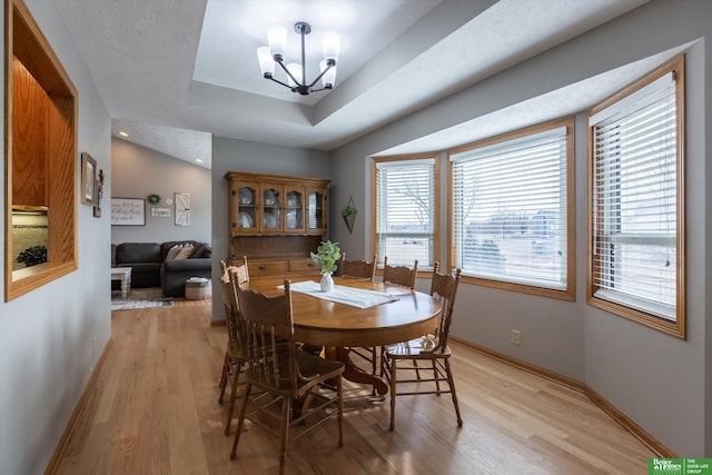 dining room featuring a textured ceiling, a notable chandelier, light wood-type flooring, and a tray ceiling