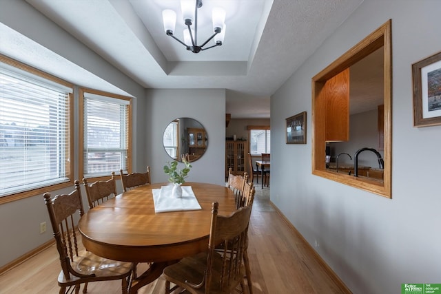 dining room with a raised ceiling, a wealth of natural light, an inviting chandelier, and light hardwood / wood-style flooring