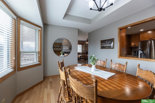 dining area featuring a tray ceiling, ceiling fan with notable chandelier, a wealth of natural light, and light wood-type flooring