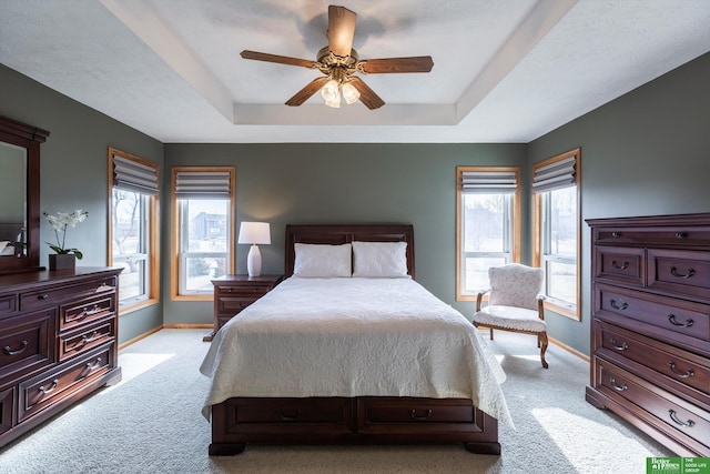 carpeted bedroom with ceiling fan and a raised ceiling