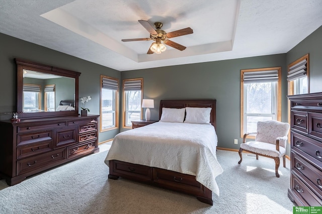 carpeted bedroom featuring multiple windows, a raised ceiling, and ceiling fan