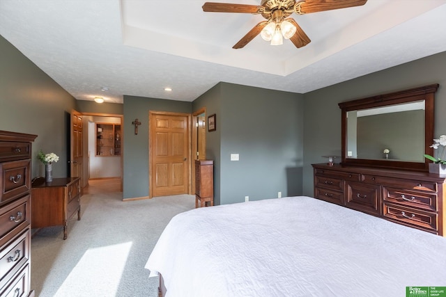 carpeted bedroom with a raised ceiling and ceiling fan