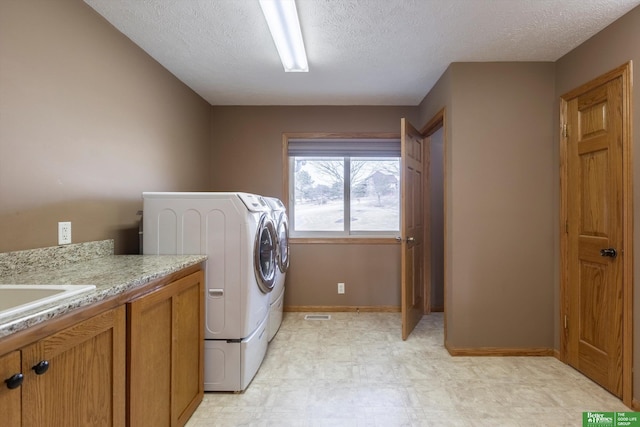 washroom featuring cabinets, sink, washing machine and clothes dryer, and a textured ceiling