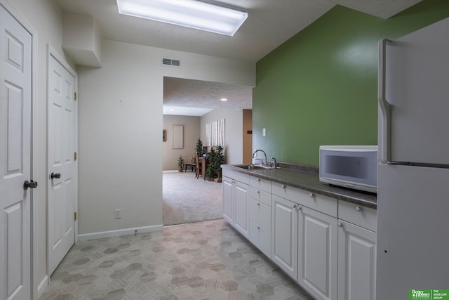 kitchen with sink, white appliances, a textured ceiling, white cabinets, and light carpet