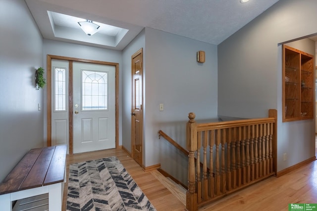 foyer entrance with a textured ceiling, light wood-type flooring, and a tray ceiling