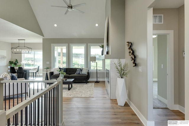 living room with ceiling fan with notable chandelier, vaulted ceiling, and light hardwood / wood-style flooring