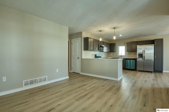 kitchen featuring dark brown cabinets, hanging light fixtures, appliances with stainless steel finishes, kitchen peninsula, and light hardwood / wood-style floors