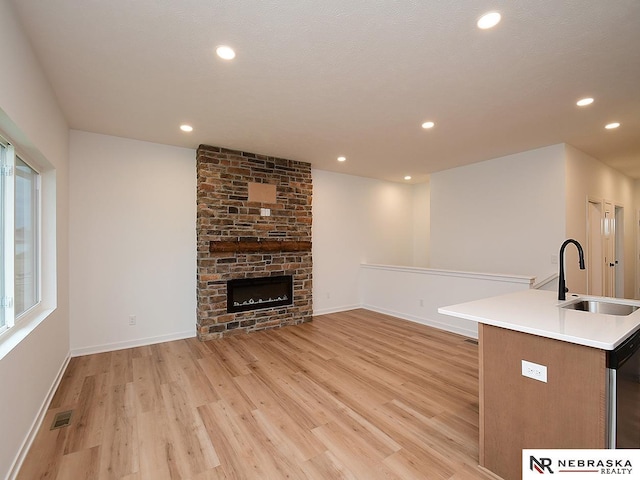 unfurnished living room with a fireplace, sink, and light hardwood / wood-style flooring