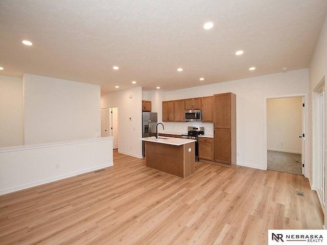 kitchen featuring sink, light hardwood / wood-style flooring, stainless steel appliances, a textured ceiling, and a center island with sink