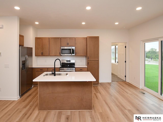 kitchen with stainless steel appliances, an island with sink, sink, and light hardwood / wood-style floors