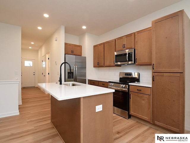 kitchen featuring an island with sink, sink, backsplash, light hardwood / wood-style floors, and stainless steel appliances