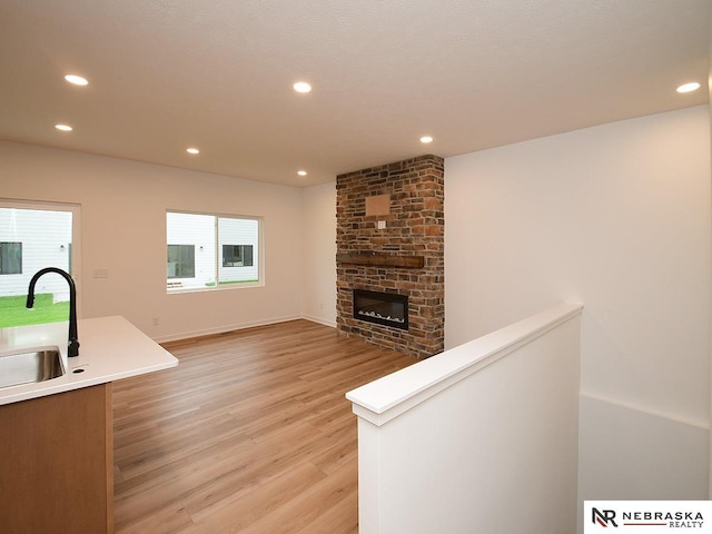 unfurnished living room featuring a stone fireplace, sink, and light wood-type flooring