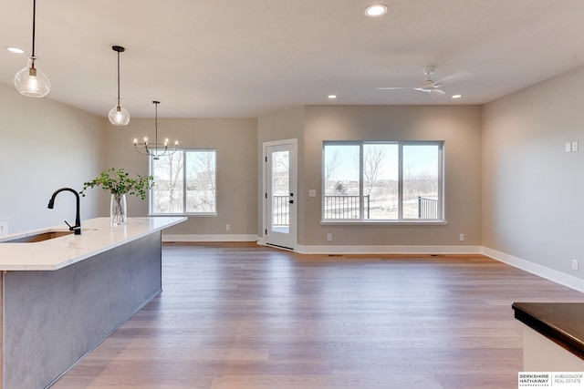 kitchen featuring sink, ceiling fan with notable chandelier, a center island with sink, decorative light fixtures, and light wood-type flooring