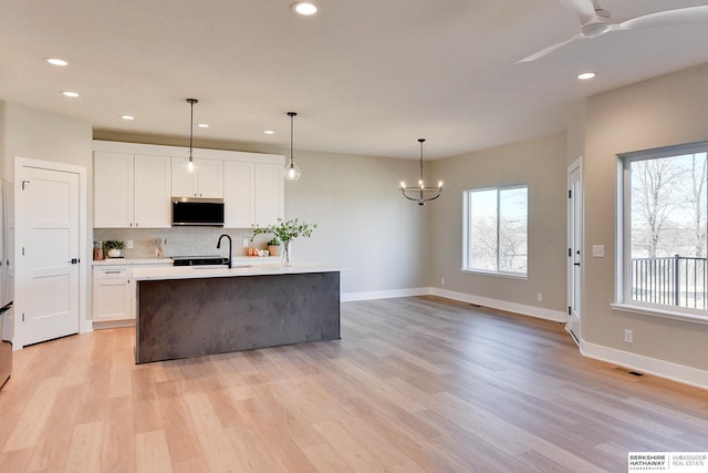 kitchen featuring sink, white cabinetry, light wood-type flooring, an island with sink, and pendant lighting