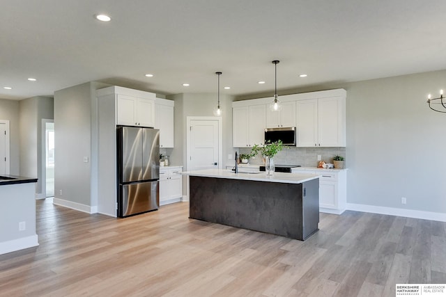 kitchen featuring hanging light fixtures, appliances with stainless steel finishes, a kitchen island with sink, and white cabinets