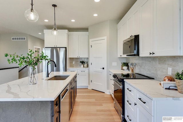 kitchen with white cabinetry, stainless steel appliances, decorative light fixtures, and a center island with sink