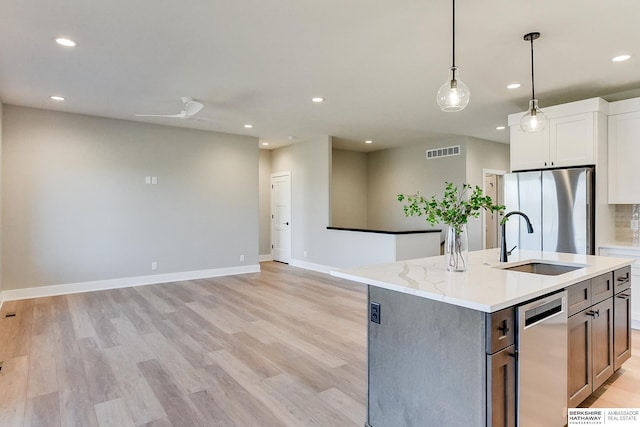 kitchen featuring pendant lighting, appliances with stainless steel finishes, light stone countertops, an island with sink, and white cabinets