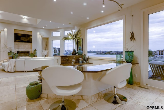 dining area with light tile patterned floors, plenty of natural light, a tile fireplace, and a water view