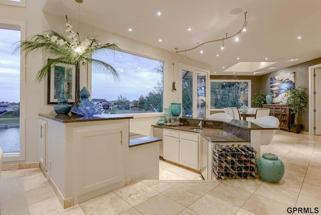 interior space featuring white cabinetry, sink, pendant lighting, and dark stone countertops