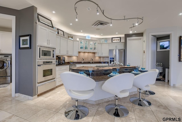 kitchen featuring appliances with stainless steel finishes, washer / dryer, decorative backsplash, and white cabinets