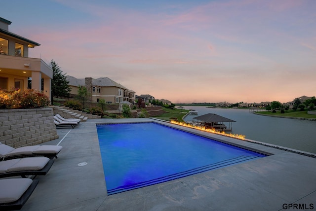 pool at dusk with a patio area and a water view