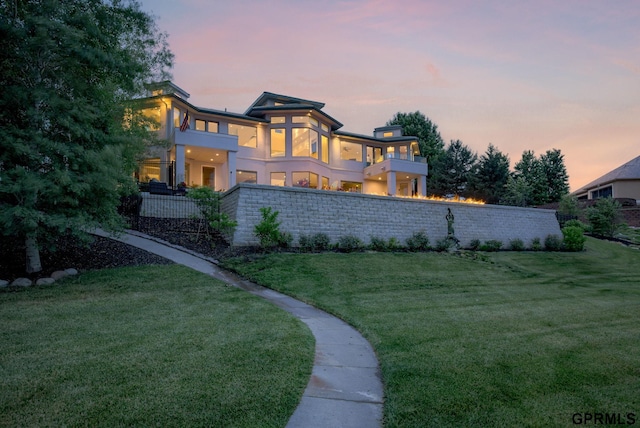 back house at dusk with a balcony and a yard