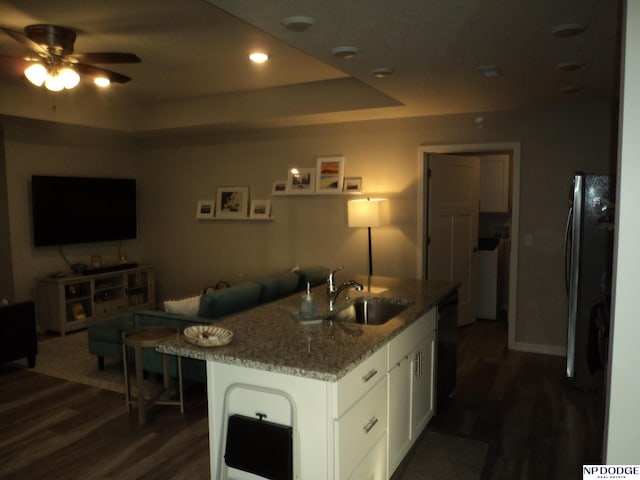 kitchen with sink, white cabinetry, stone countertops, a raised ceiling, and a kitchen island with sink