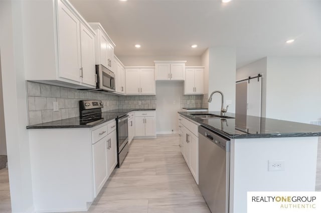 kitchen featuring sink, appliances with stainless steel finishes, white cabinets, a center island with sink, and a barn door