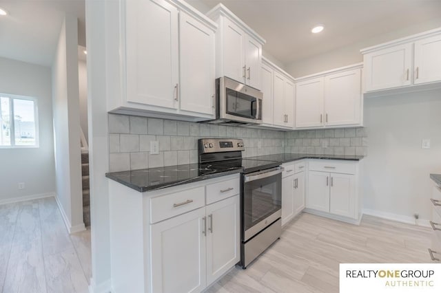 kitchen featuring white cabinetry, stainless steel appliances, dark stone countertops, and backsplash