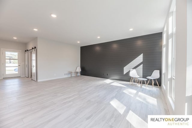 unfurnished living room with wooden walls, a barn door, and light wood-type flooring