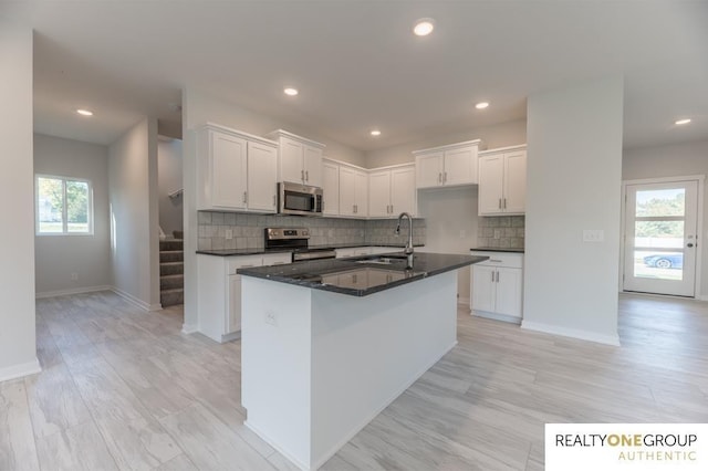 kitchen with sink, appliances with stainless steel finishes, a kitchen island with sink, tasteful backsplash, and white cabinets