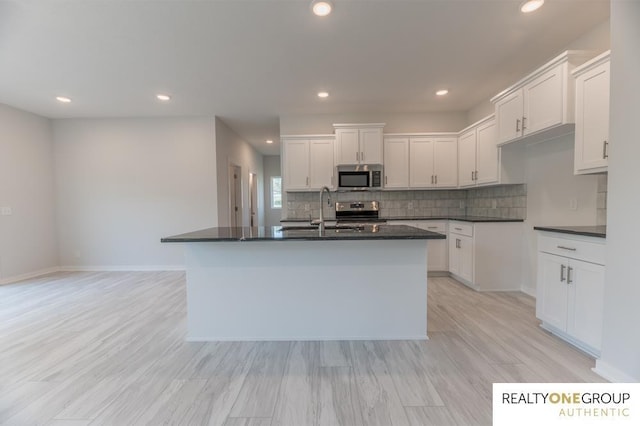 kitchen with sink, white cabinetry, a center island with sink, light hardwood / wood-style flooring, and appliances with stainless steel finishes