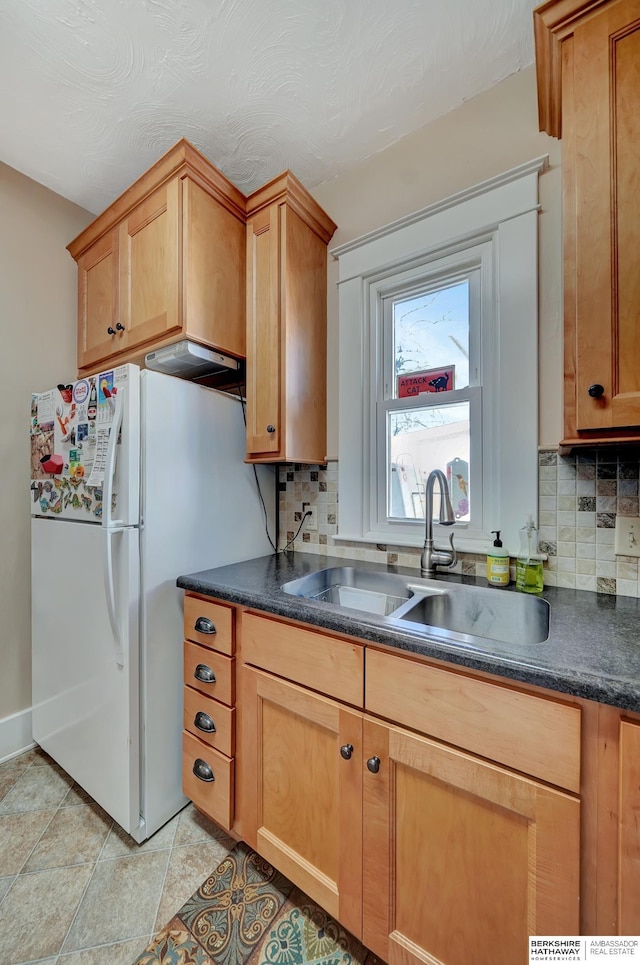 kitchen with light tile patterned floors, sink, white fridge, and backsplash