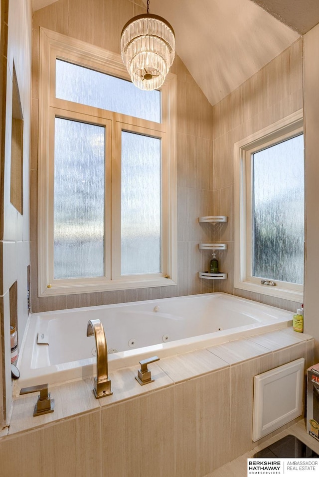 bathroom featuring a notable chandelier, vaulted ceiling, and tiled bath