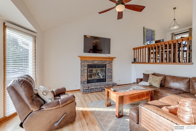 living room featuring vaulted ceiling, ceiling fan, a fireplace, and light wood-type flooring