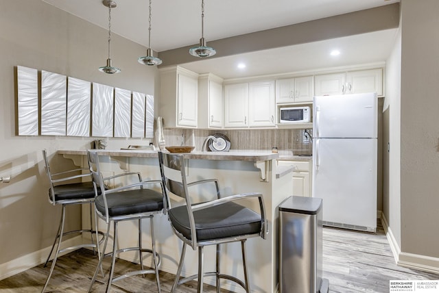 kitchen featuring white appliances, decorative backsplash, white cabinets, a kitchen bar, and decorative light fixtures