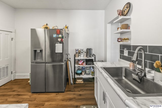 kitchen with sink, dark wood-type flooring, stainless steel fridge, light stone countertops, and white cabinets