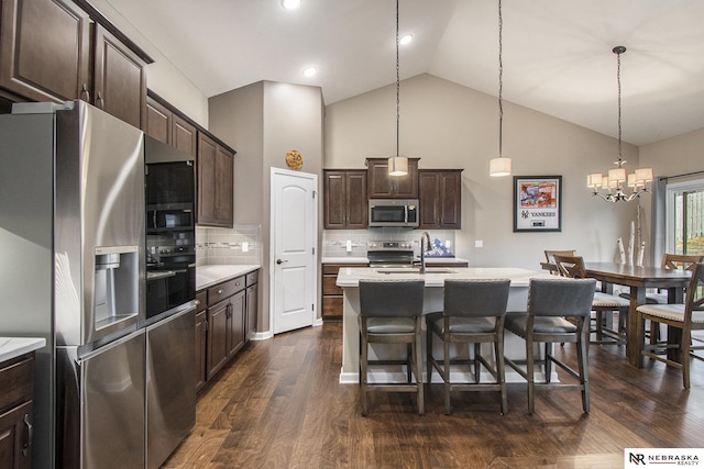 kitchen with pendant lighting, backsplash, stainless steel appliances, dark brown cabinetry, and an island with sink