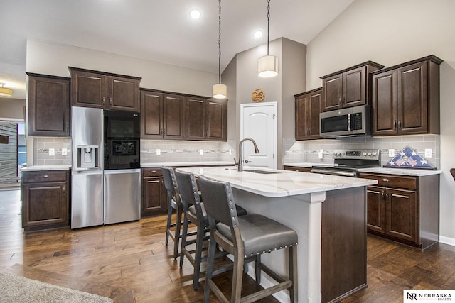 kitchen with appliances with stainless steel finishes, high vaulted ceiling, sink, a kitchen breakfast bar, and a kitchen island with sink