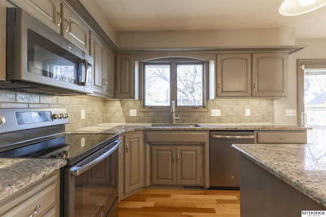 kitchen with sink, light stone counters, light hardwood / wood-style flooring, stainless steel appliances, and decorative backsplash