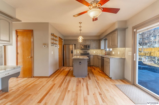 kitchen featuring gray cabinetry, appliances with stainless steel finishes, a kitchen island, light stone countertops, and decorative backsplash