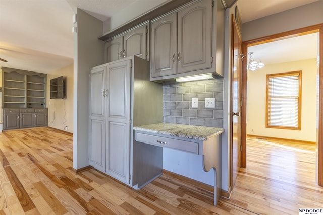 kitchen featuring light stone counters, gray cabinetry, light wood-type flooring, and backsplash