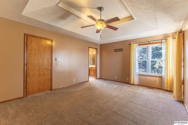 unfurnished bedroom featuring a raised ceiling, connected bathroom, a textured ceiling, and ceiling fan