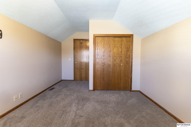 unfurnished bedroom featuring carpet flooring, vaulted ceiling, and a closet