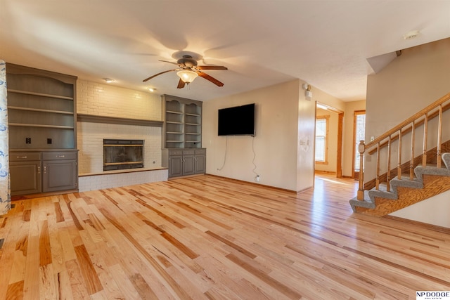 unfurnished living room featuring ceiling fan, a fireplace, and light wood-type flooring