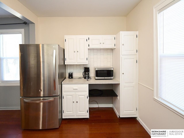 kitchen with dark wood-type flooring, appliances with stainless steel finishes, white cabinetry, backsplash, and built in desk