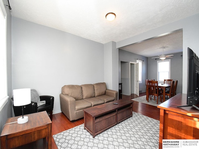 living room with ceiling fan, a textured ceiling, and light wood-type flooring