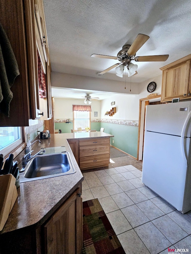 kitchen featuring freestanding refrigerator, light countertops, a textured ceiling, a sink, and light tile patterned flooring