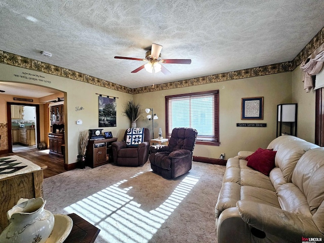 living room with carpet, a textured ceiling, arched walkways, and a ceiling fan