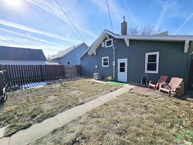 back of property with a fenced backyard, a chimney, central AC unit, and a lawn